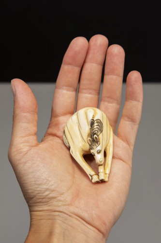 An ivory netsuke depicting a horse with lowered head and joined legs - 