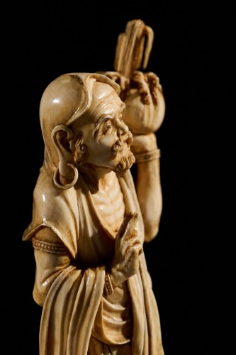 Asian Works of Art  - An Ivory Okimono Of A Rakan Holding A Ritual Vase, Signed Kazutoshi