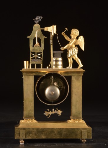 Antiquités - Cupidon forgeron - Pendule portique en bronze patiné et doré au feu d’époque Empire,