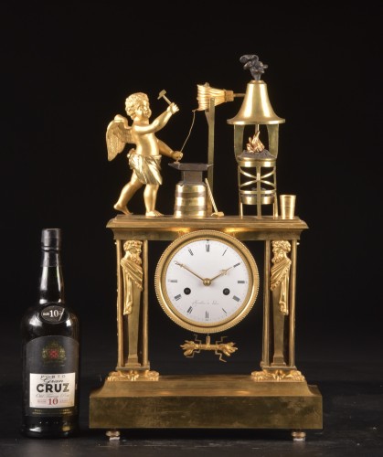 Antiquités - Cupidon forgeron - Pendule portique en bronze patiné et doré au feu d’époque Empire,